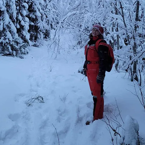 Kvinne i rød vinterdress smiler på sti omgitt av snøtunge trær.